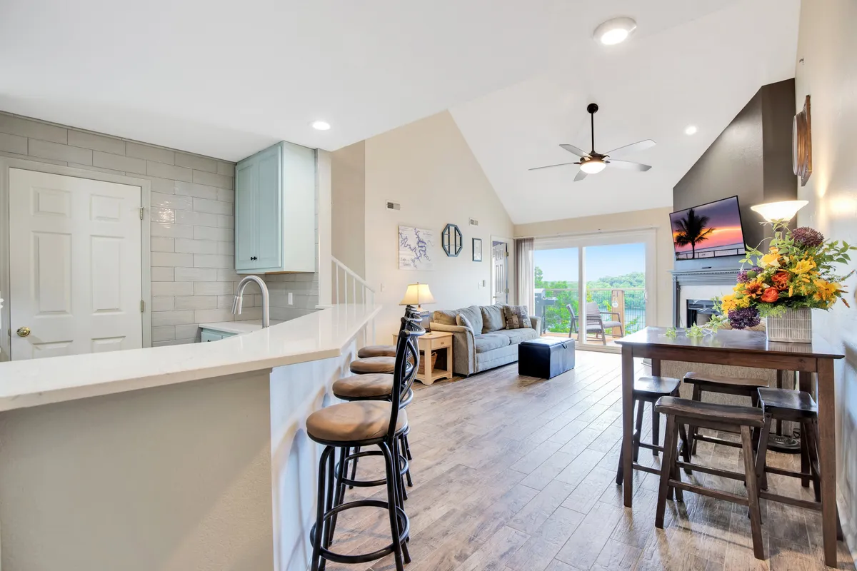An open-concept kitchen and living area with a kitchen island, ample living room seating, and large windows that flood the space with light and provide a beautiful view of the outdoors. The setup seamlessly connects the kitchen with the social spaces, ideal for gatherings and shared meals.