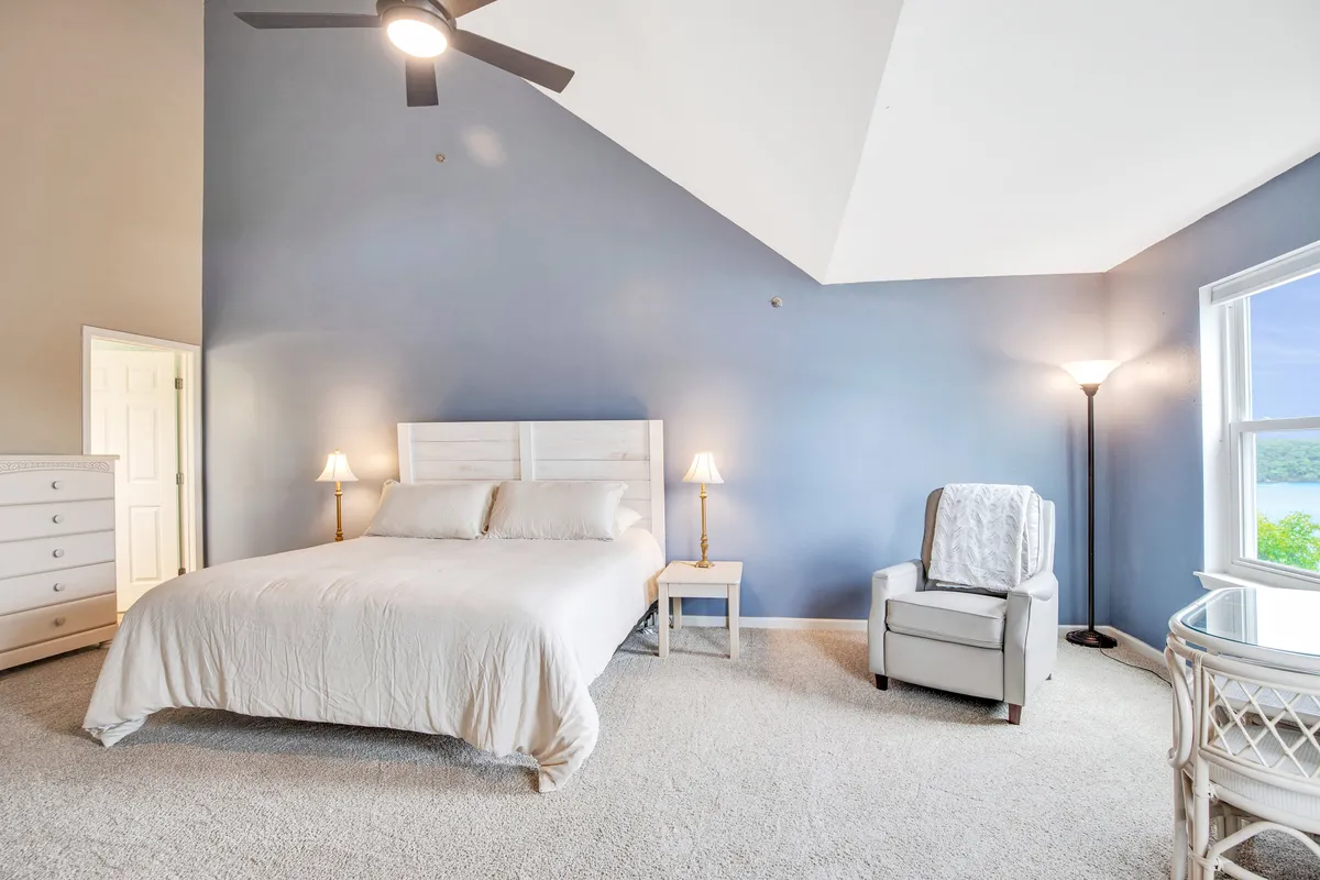 A cozy bedroom highlighted by a comfortable bed, an inviting armchair placed by a window, a nightstand with a reading lamp, and gentle morning light entering the space. The atmosphere signals a retreat where one can relax, read, or simply enjoy quiet moments alone.