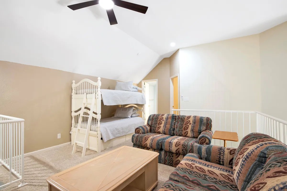 This image features a welcoming loft-like space with bunk beds, a sofa set, and a coffee table. The arrangement creates a cozy, inviting atmosphere ideal for children to relax, read, play games, and spend quality time together. The presence of bunk beds and a dedicated play area clearly signals that this is a space designed with children's needs and safety in mind.