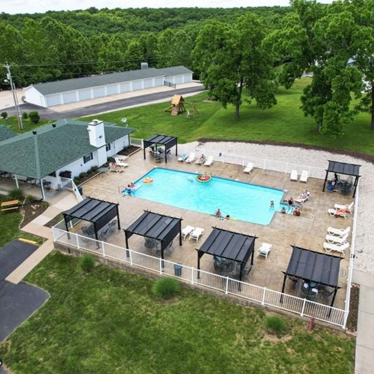 This image showcases the community swimming pool surrounded by cabana structures, a lush green lawn, and mature trees. The pool area looks inviting, with plenty of space for swimming, sunbathing, and social gatherings. The relaxed atmosphere is perfect for family fun and poolside activities.