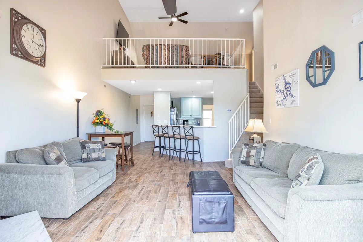 A cozy, well-lit interior with sofas, a dining table, a visible kitchen area, and a staircase. The space is arranged for comfort and sociability, perfect for movie nights, game sessions, and group dining, reflecting the versatility of the gathering haven.