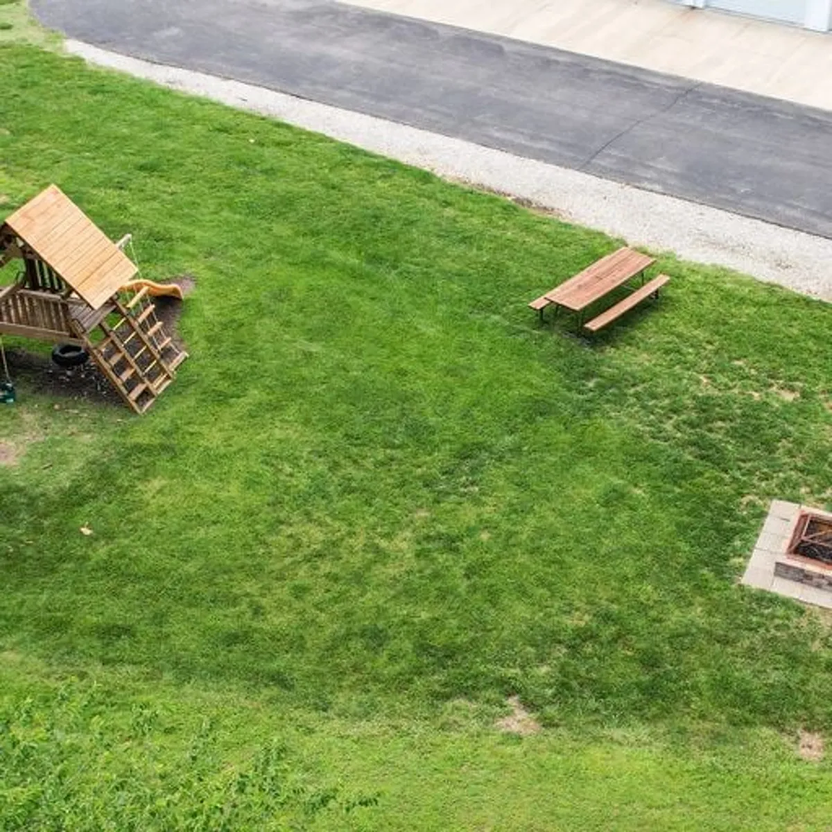This outdoor scene captures a vibrant playground structure, a picnic table, and a fire pit area, all set within a lush green space. The setting is ideal for children to play and for families to gather, reinforcing the family-friendly environment.