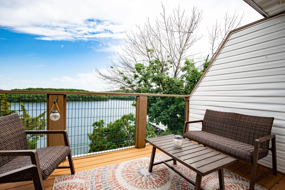 The image features a cozy outdoor seating arrangement with wicker chairs and a coffee table, all facing a stunning view of the lake. The inviting setup is ideal for morning coffee, evening gatherings, and soaking up the natural beauty.