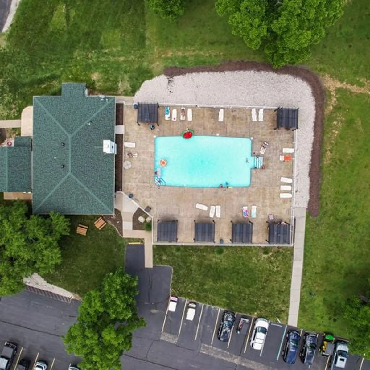 An inviting exterior scene featuring a swimming pool bordered by lounge chairs, with the residential building and green trees in the background. The atmosphere is leisurely and social, perfect for relaxation or gathering with neighbors.